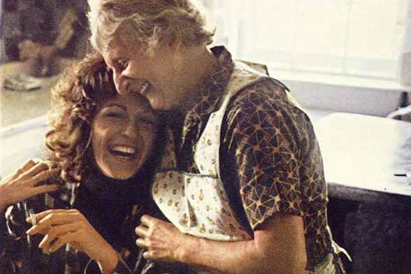 1971 

A candid photograph capturing a moment between two individuals, one in an apron and the other with curly hair.
The setting appears to be indoors.
Tags: vintage, candid photo, indoor scene, joyful expression
