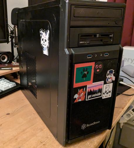 A photo of the aforementioned sub-50 dollar PC.

It's a well-used SilverStone mini-tower chassis, all black with some vent meshes front and side.
It has a DVD multi-burner in the first 5.25 inch bay, a combination floppy drive and card reader in the second 5.25 inch bay through a 3.5 inch adapter and a bunch of stickers, mostly furry ones, on the front of the system.