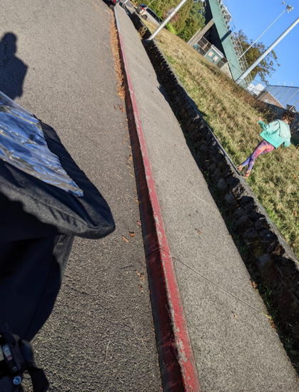 Kid running along a low wall, long shadow of me and the cargo bike as I ride alongside