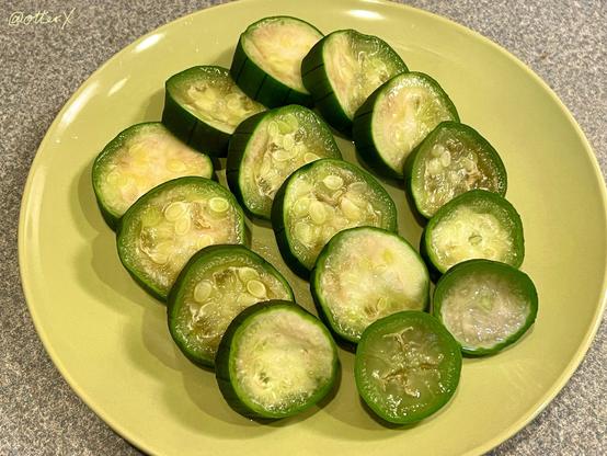 Sliced and lightly-boiled luffa gourd neatly placed on the avocado-green plate on the gray counter. They look like cooked zucchini slices.