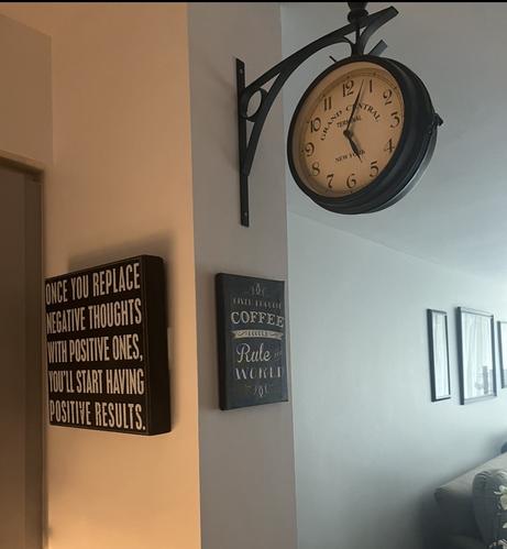 Photo of a corner kitchen wall. There’s a black sign with white text that reads “once you replace negative thoughts with positive ones you’ll start having positive results”. A second black sign with white texts reads “given enough coffee I could rule the world”. Above that sign is a wall clock that has the words New York grand central terminal on it.
