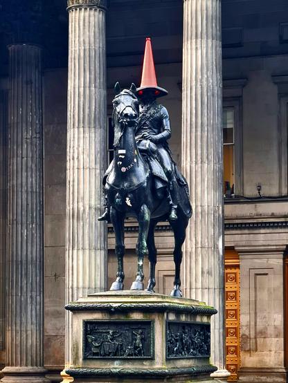 A statue of the Duke of Wellington with a road cone on his head that makes it look like he has red glowing eyes.