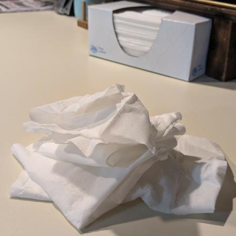 A pile of used tissues on the counter in the foreground with a box of tissues in the background.