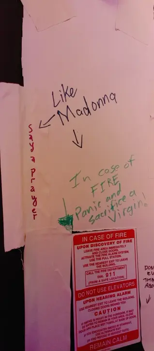 It says "Say a prayer" and "In case of FIRE panic and sacrifice a virgin." Over both these messages has another one saying "Like Madonna" and two arrows pointing to the two previous messages.