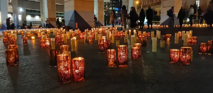 A picture of a sea of candles. There are some people in the background and concrete columns. Since it's under a highway.