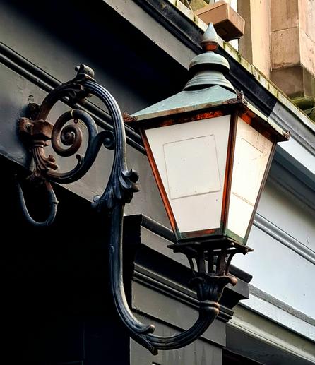 An ornate old gas lamp above the entrance to a small pend running under an old building.