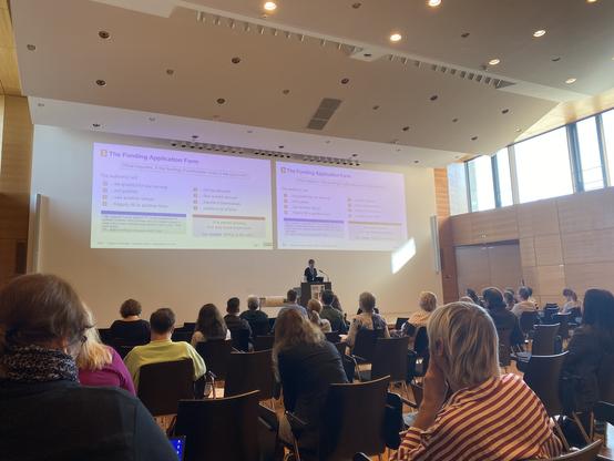 Foto von der openCost-Konferenz in Regensburg. Gezeigt würd die Bühne mit dem Sprecher und seinen Folien.