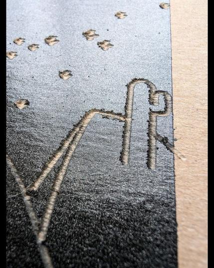 A desert landscape at night is engraved into black-painted paperboard, revealing the natural texture beneath. The scene features a crescent moon above flowing dunes, with a cactus in the foreground. Stars are scattered across the sky as textured indentations. The contrast between the rugged engraved lines and the smooth black background creates a striking depiction of the quiet beauty of the desert at night.  Close-up views reveal the intricate grooves of the moon, stars, and cactus, adding depth. The handcrafted nature of the engraving offers a tactile, raw representation of solitude and serenity. It reflects the stark beauty of the desert and the stillness of the night, made more striking by the handcrafted nature of the engraving—each line and star invites touch and carries the weight of quiet solitude.