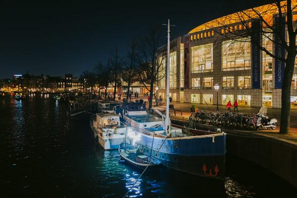 A ship has a lit up sign saying "Hope" on it. The ship is moored by a large building in Amsterdam.