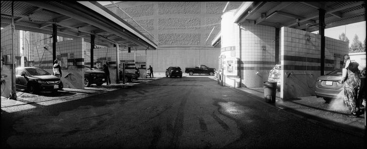 A view down the alley of car wash stalls as people sud and rinse their vehicles.