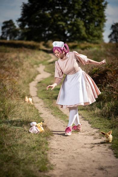 cosplay of nurse joy from pokemon, togehter with an evee, mew and pikachu in a field of fern