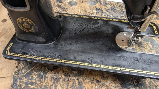 antique cast-iron Pfaff sewing machine after sanding the base after the first coat of black shellac paint. The surface has become scratched up from the sanding, but the areas with missing paint are still lower than the rest of the paint, although they are already mostly black and not bare metal.