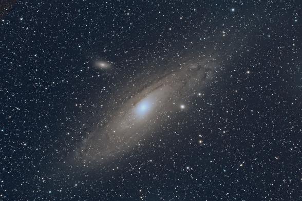 Foto der Andromeda Galaxie. Die Rotationsebene der Galaxie steht in etwa entlang der Bilddiagonalen von links unten nach rechts oben.
In etwa der Mitte der Galaxie etwas links oberhalb sieht man eine weitere visuell kleine Galaxie.

Es sind ein paar Strukturen der Galaxie zu sehen, etwas dünklere Stellen die um das Zentrum in verschiedenen Radien die Spiralarme abgrenzen.
Die Farbe ist etwas gelblich.