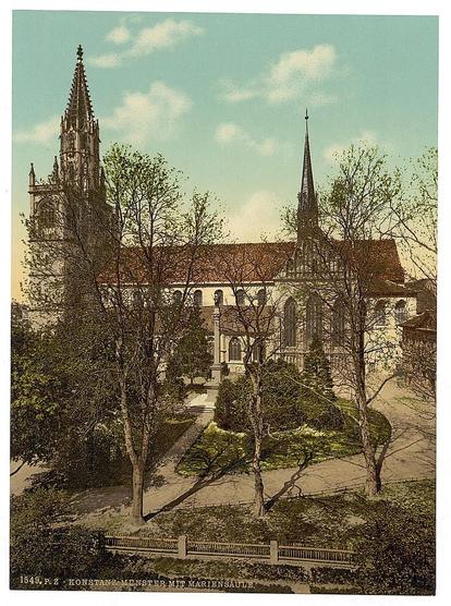 The image depicts a historic church with prominent Gothic architectural elements, including pointed spires and large windows. The building is surrounded by mature trees that add to its serene ambiance. In the foreground, there's a well-maintained garden area with benches, suggesting it might be a place for contemplation or leisurely walks. A path winds through the greenery, leading towards the church entrance visible in the mid-ground of the composition.

The image has been colored and printed on paper using the Photochrom process, which was popular during the late 19th to early 20th centuries. This technique involves capturing images with a cyan, magenta, yellow filter, creating vibrant colors that were not achievable through traditional printing methods at the time. The coloration gives an impression of what the location might have looked like in its prime.

The image includes text indicating it is from Konstanz's church with Mary on the roof (Konstanz Münster Mit Marienau). A date range, approximately 1890 to 1900, suggests when this photochrom print was produced. This particular work by Loe Nier shows how historical sites were preserved and presented in art forms accessible to a broader audience during that era.

This photograph serves as a valuable cultural artifact, showcasing the architectural beauty of Germany's Baden region and offering insight into photographic  [...]