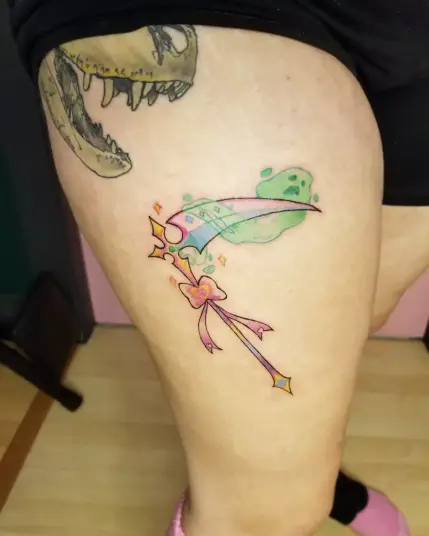 Photo of a tattoo i designed and did on myself. It's a pastel multicoloured magical girl necromancer scythe, with a spirit wrapped around the blade.