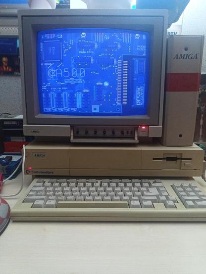 Un moniteur 1081 posé sur un Amiga 1000, avec un clavier en premier plan et un classeur "Amiga" posé à côté du moniteur. Le moniteur affiche une carte-mère d'Amiga 500 avec une carte d'extension sur laquelle est écrit "DESIRE", le nom du groupe ayant fait la démo.