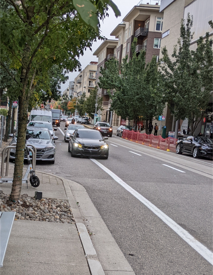 An amazon truck and two cars parked in the bike lane on S Bond, the UPS truck right before a marked crosswalk, obstructing visibility of people crossing from behind the truck.  A person on a bike is approaching, having already gone around the truck, a car behind them and another in the extra car lane, about to go around the two double-parked cars
