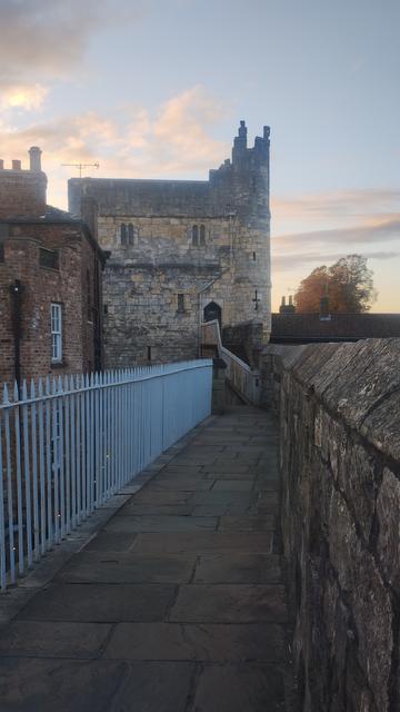 Looking along the walkway of the medieval city walls at dusk, towards a large, stone gatehouse