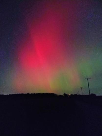 The Aurora 
Bright red up centre and top, green under and to the lower right
A bit of curtaining seen and the silhouette of telephone wires along the road on the bottom right