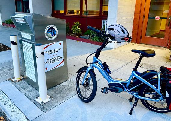 At the City of Monterey Public Library, a blue Tern NBD bicycle is parked alongside a County of Monterey, California official ballot drop box (with text in Spanish and English). This is one of nineteen 24-hour  official ballot drop boxes around Monterey County. 

A beige bike helmet rests atop the bicycle’s handlebar. The helmet has a sticker “I voted by mail.” (All California active registered voters will receive a vote-by-mail ballot for the November 5, 2024, General Election. Vote-by-mail ballots can be returned by mail, at a drop-off location, or your county elections office.)