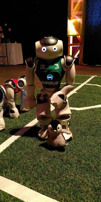 Archy is sitting in front of a standing soccer robot. The robot is about 5 times the size of Archy.