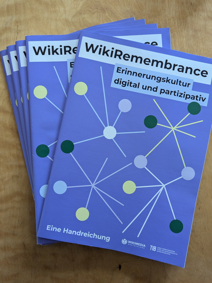 Auf einem Tisch liegender Stapel der Handreichung "WikiRemembrance - Erinnerungskultur digital und partizipativ". Zu sehen sind der Titel sowie die Logos der HerausgeberInnen TIB und Wikimedia Deutschland.