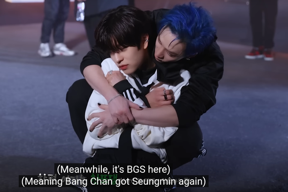 On the set of the Maniac music video, Bang Chan hugs Seungmin tightly from behind while they both sit on the ground. Caption reads: (Meanwhile, it's BGS here) (Meaning Bang Chan got Seungmin again)