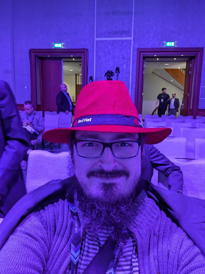 Me sitting with red fedora from the redhat booth after coffee break while people are slowly starting to gather back in the main stage
