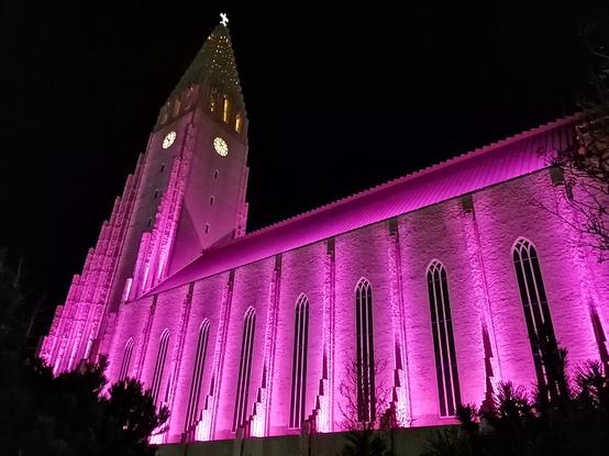 Une vue de côté de l'église. Les murs et la toiture sont colorés par des lumières roses.