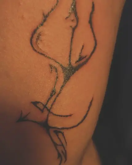 An image of a tattoo on somewhat olive skin, a black sigil that's difficult to describe but which has a trident shape and hugs the inner knee area, extending in four directions with intuitively drawn lines accenting its curved