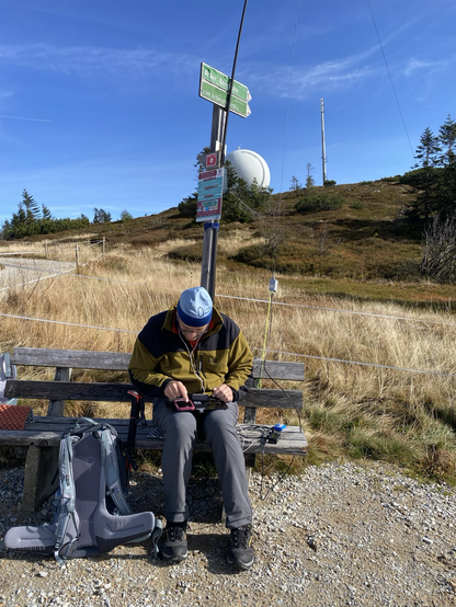 A man sitting on a bench with a portable radio station and a radome in the background