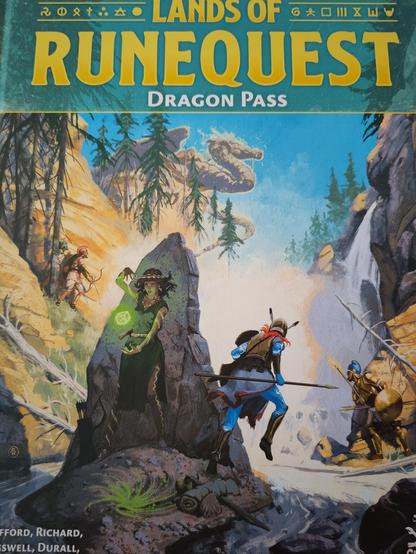 (runes) Lands of (runes)
       R U N E Q U E S T
          Dragon Pass

Picture of a gorge with various people in ancient looking dress with Spears and shields. An Archer on the cliffs on left. All are looking up at a waterfall. Overlooking the waterfall is a dragon like creature.

In the foreground, in the shadows of a monolith, is a woman in a green dress preparing some magic. A green glow shines from between her raised right hand and lower left hand.