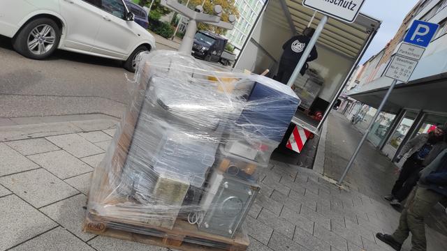 Im Vordergrund eine folierte Palette. Im Hintergrund wird auf der Ladefläche eines LKW eine zweite Palette bereitgestellt. Rechts das SpoSo-Gebäude in Neu-Ulm.