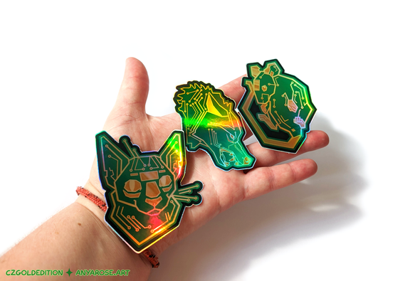 Hand holding three holographic vinyl stickers designed to look like animals made out of printed circuit boards - a cat, snarling wolf, and mouse.