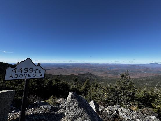 Picture from Whiteface mountain at 1371.3m. We see the mountains in the distance and there is a sign to the left indicating the altitude. 
- - -
Photo à partir du mont Whiteface à 1371,3m. Il y a des montagnes dans la distance et une pancarte à la gauche indiquant l’altitude.