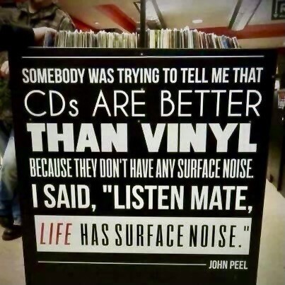 A display with a humorous quote by John Peel emphasizing the charm of vinyl records over CDs, stating that "Somebody was trying to tell me that CDs are better than vinyl because they don't have any surface noise. I said, 'Listen, mate, life has surface noise.’" The background shows rows of records.