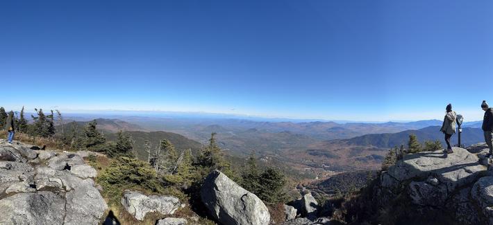 The view to the east (towards the state of Vermont):

We can see mountains left, right and centre. The trees are green and orange hues. There is a stream of clouds very far away. 

Near the photographer, you can see the mountain dropping down into the valley.
- - -
Vue vers l’est (direction de l’état du Vermont): 

On peut voir des montagnes dans toutes les directions. Les arbres sont dans des teintes de vert et d’orange. Il y a une ligne de nuages très loin. 

Proche du photographe, on peut voir la montagne “tomber” dans la vallée.