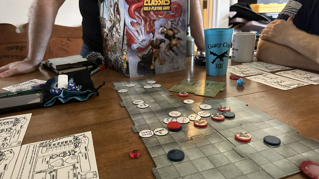 A battle map, with tokens representing characters on it. An XCC gm screen appears in the background.