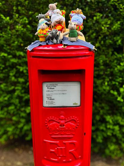 A red British postbox with a knitted family of mice on top of it.