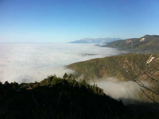 Wide iPhone landscape photo of BigBear that features green mountains & a huge valley filled with heavy fog with a clear blue sky above