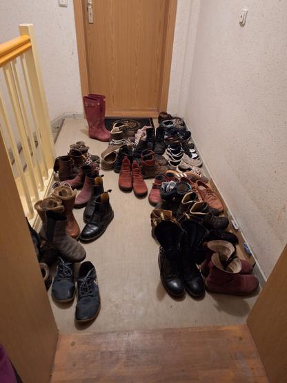 In einem Hausflur/Treppenaufgang stehen mehr als 23 paar Herbstschuhe.