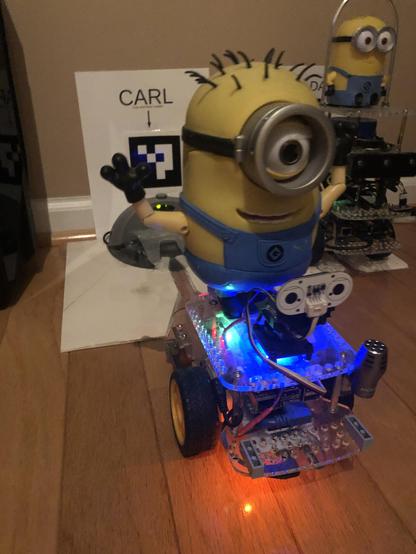6 year old robot Carl is a GoPiGo3 mobile robot platform with a tall rubber Minion Carl on top, shown in front of his recharge dock.