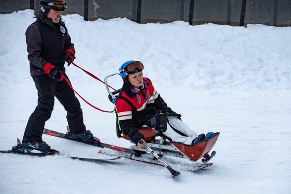 Me, steering sitski with outrigger poles & my instructor skiing & holding safety straps behind me. It was my 1st sitski fun race. Going into a turning move.