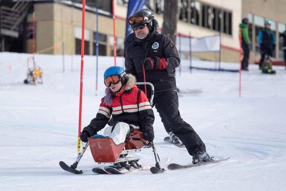 Weaving through poles in my first sitski trial race.
Me, steering sitski with outrigger poles & my instructor skiing & holding safety straps behind me. It was my 1st sitski fun race.