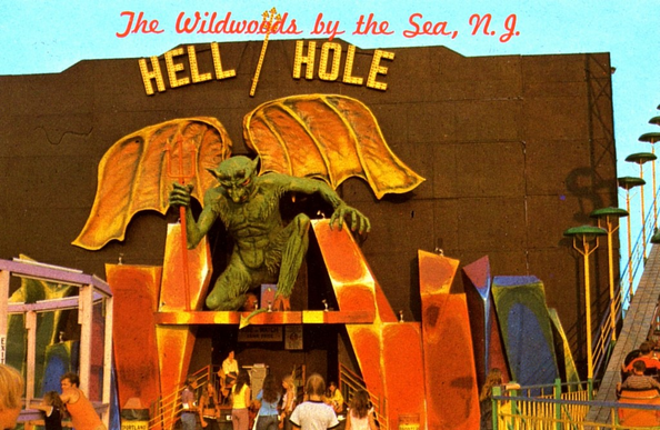 Fotografía real de lo que parece una casa del terror, no estoy segura porque es en inglés. Arriba hay un cartel sobre la atracción que dice "The Wildwoods by the Sea, N.G. Hell / Hole". Hay una gárgola sosteniendo un tridente rojo en la puerta y gente haciendo cola.