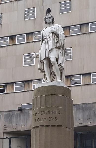 Photo of a classical-style Christopher Columbus statue on a pedistal in front of a courthouse on Brooklyn's Borough Hall. There is a black pigeon sitting atop Mister Columbus's head.
