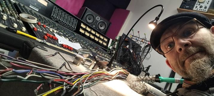Bearded dude selfie in front of large mixing desk. Soldering iron and multi cable in front