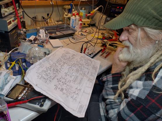 Bearded dude looking at schematics in electronics lab. Bread board on the work table