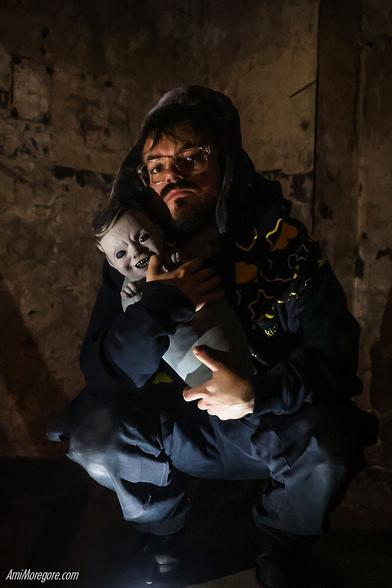 Lil Kevo 303 squatting in a squallid room while clucthing what appears to be a baby vampire
