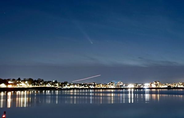 seaside scene with a comet being photobombed by the flashing red lights of an aeroplane taking off below it